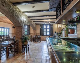 Un restaurante con paredes de ladrillo visto, vigas de madera y una zona de bar con mostrador de vidrio.
