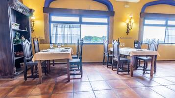 Zona pranzo con tavoli e sedie in legno, pavimento piastrellato e vista dalle finestre.