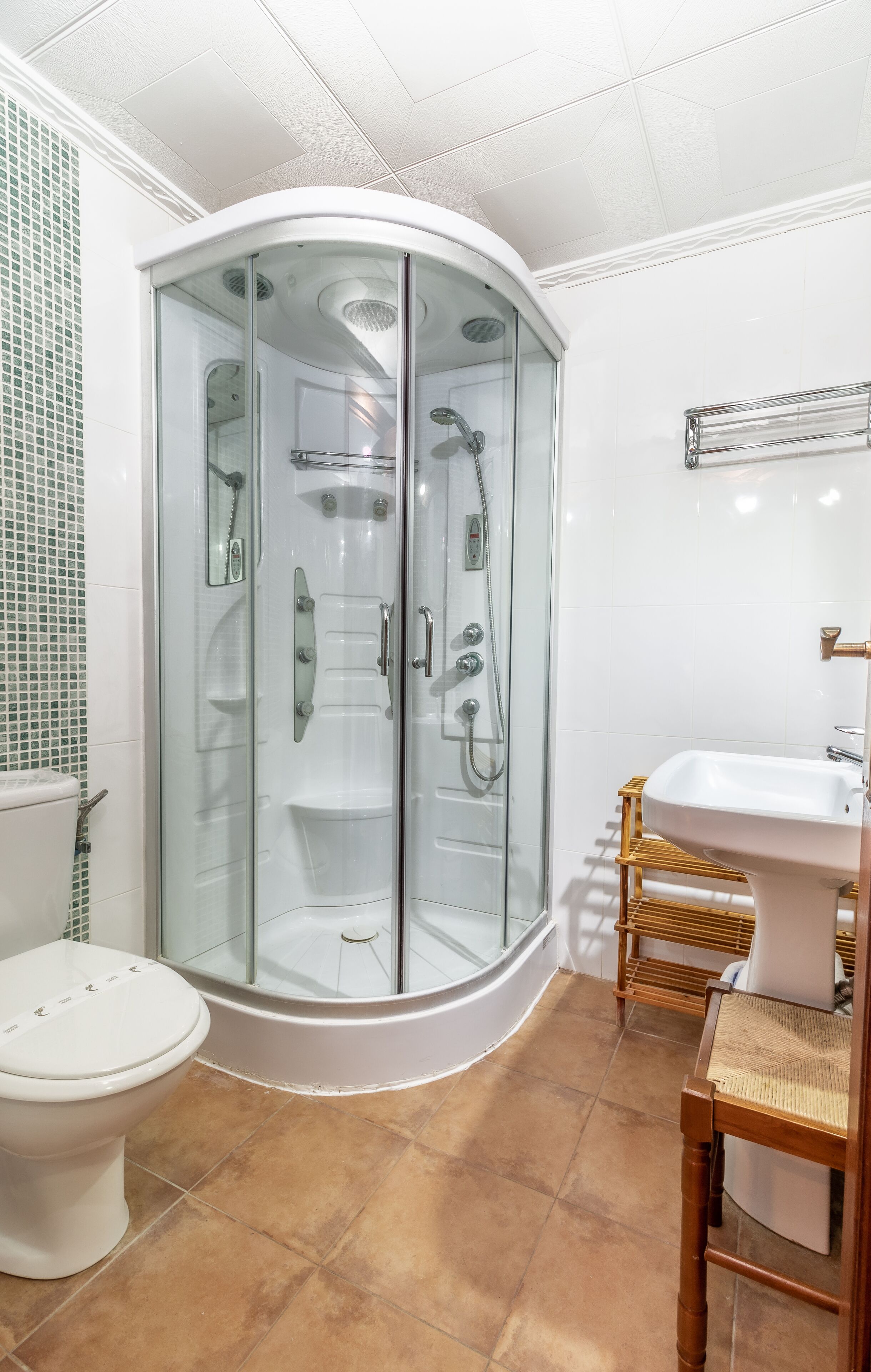 Un baño moderno con cabina de ducha de vidrio, un inodoro blanco y una silla de madera.