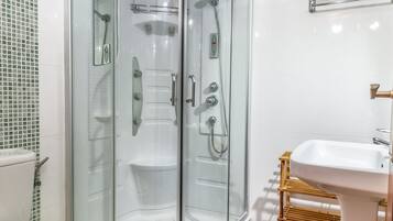 Un baño moderno con cabina de ducha de vidrio, un inodoro blanco y una silla de madera.