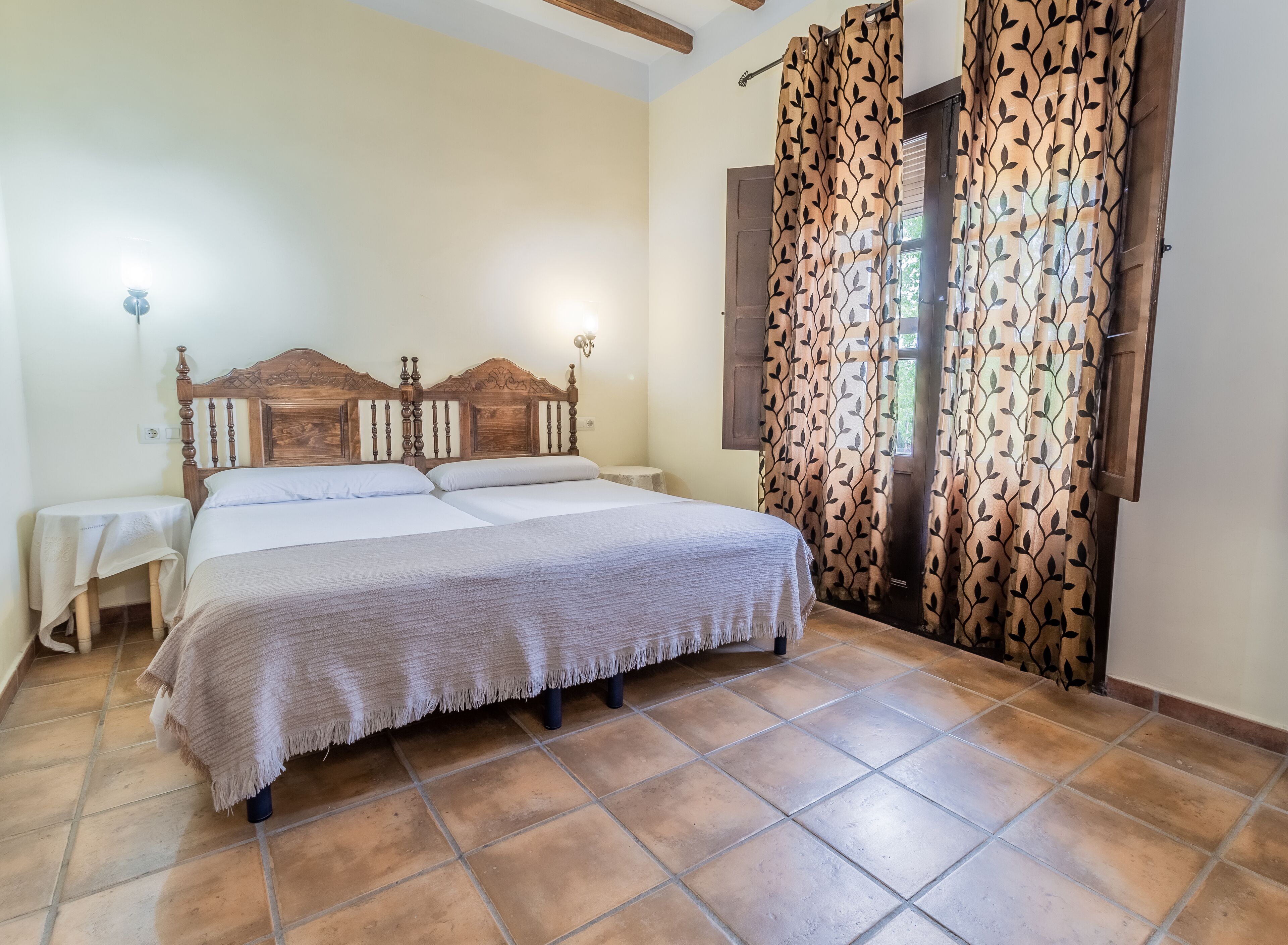 A double bed with a wooden headboard, two bedside tables, and a patterned curtain.