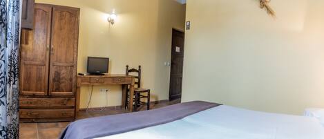 A bedroom with a bed, a desk with a computer, a wardrobe, and a door.