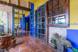 Un pasillo amplio con suelo de baldosas, pared de ladrillo y una puerta azul que da a otra habitación.
