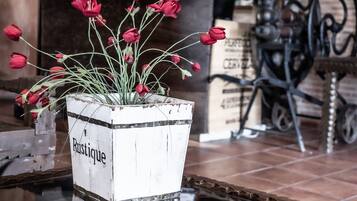 Ein rustikaler Blumentopf mit roten Blüten auf einem Glastisch in einem Raum mit Backsteinwänden und einem Holzregal im Hintergrund.