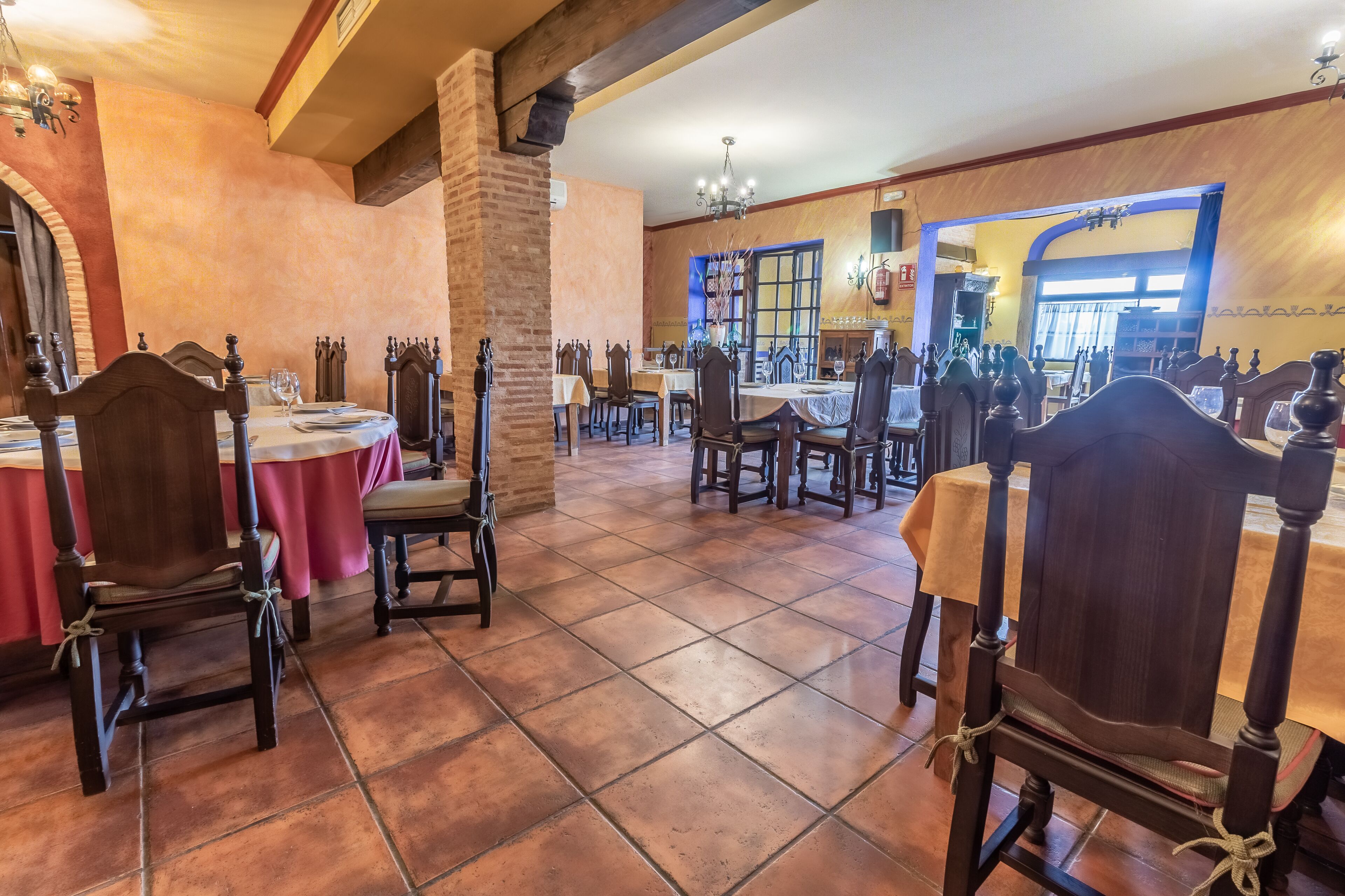 A dining area with wooden tables and chairs, a brick column, and a tiled floor.