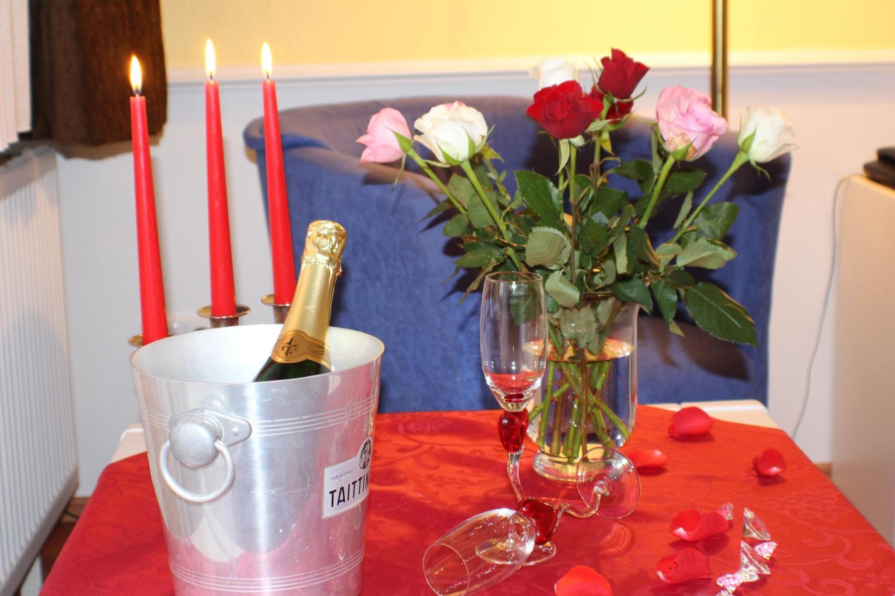 A table with a red tablecloth, a metal bucket labeled "Taitting," a glass with a rose, and red candles.