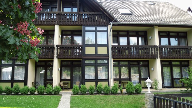 A multi-story building with balconies, a garden with small shrubs, and a pathway leading to the entrance. - Landhotel Combecher (Neukirchen)