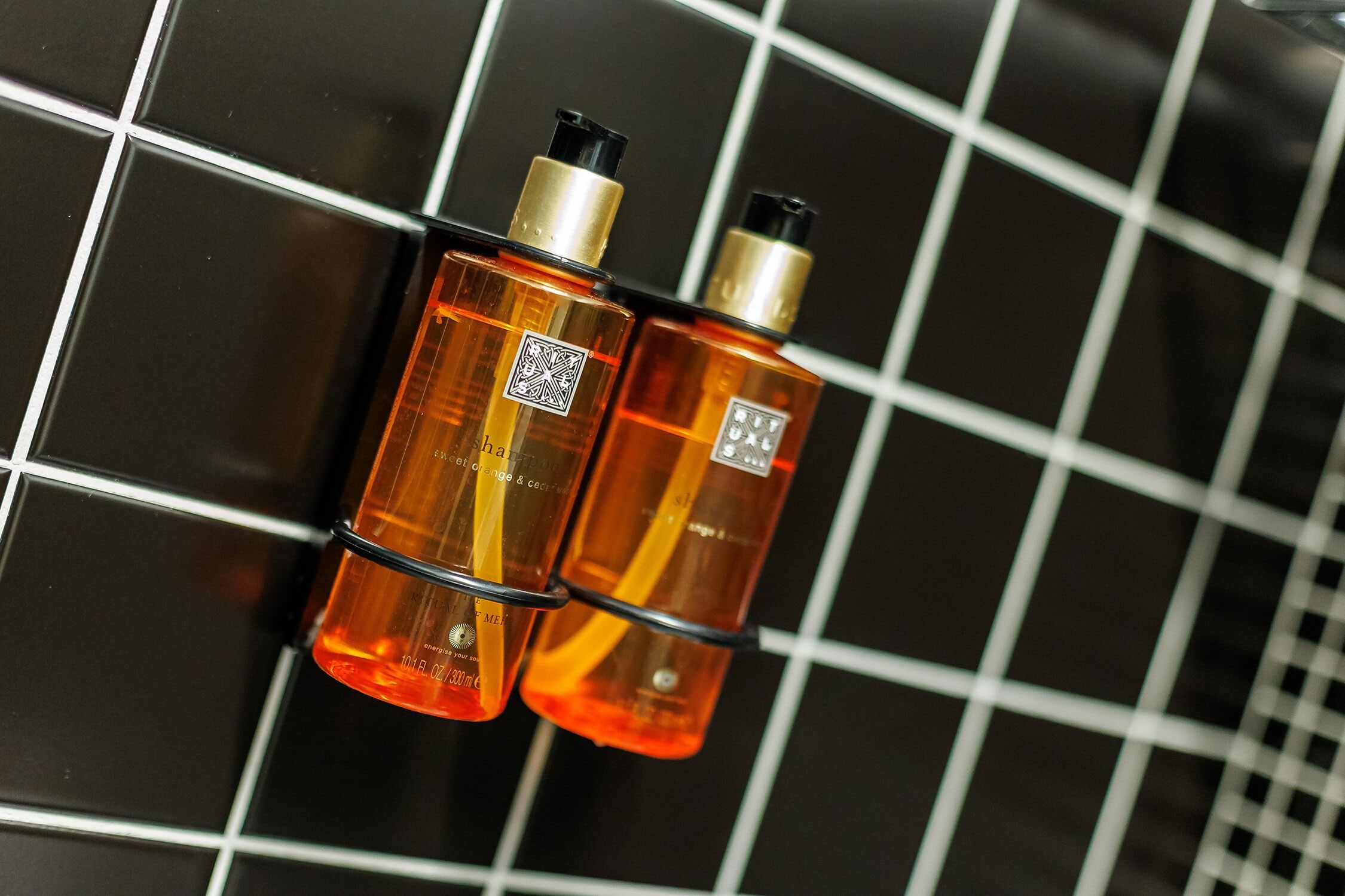 Two bottles of perfume hanging on a tiled wall.