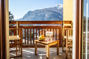 A wooden balcony with a table and chairs, a bottle of wine, and a fruit bowl. A mountain is visible in the background. - Crabun (Pont-Saint-Martin)