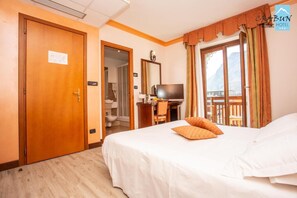A hotel room with a bed, a desk with a TV, a bathroom visible through an open door, and a balcony with curtains. - Crabun (Pont-Saint-Martin)