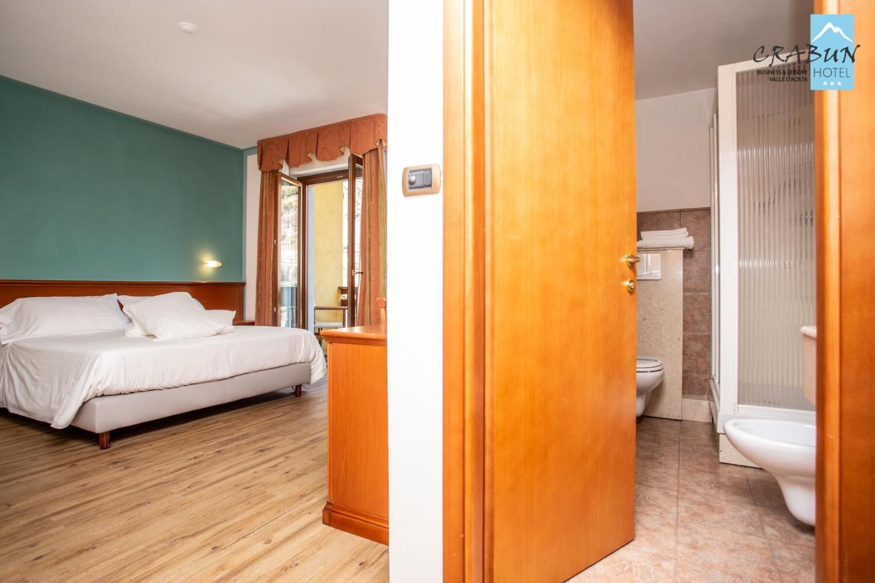 A hotel room with a bed, a wooden door, and a bathroom with a toilet and sink.