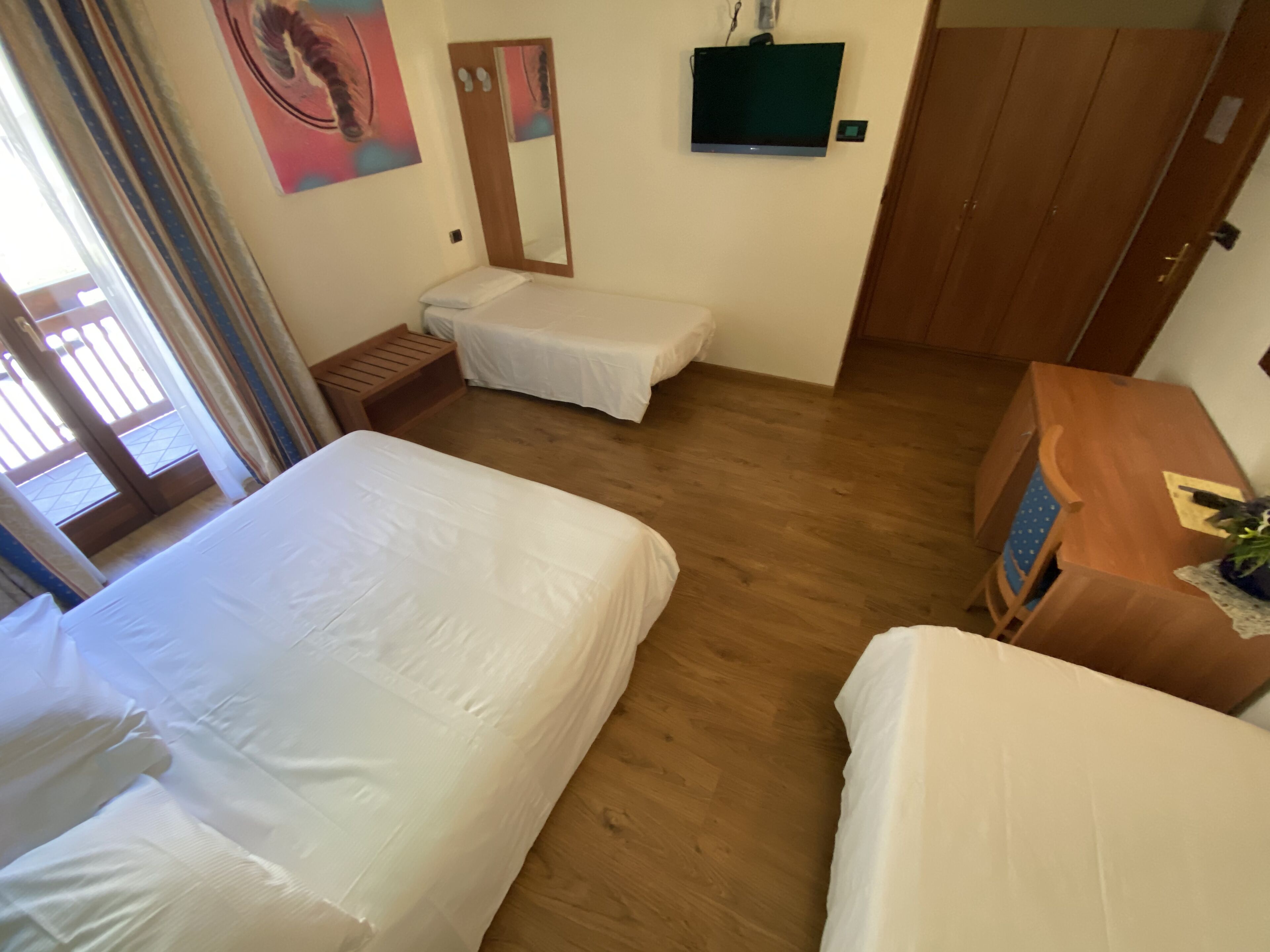 Een hotelkamer met twee bedden, een houten vloer, een aan de muur bevestigde televisie en een houten kledingkast.