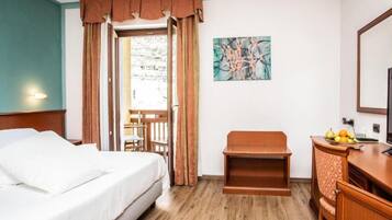 A hotel room with a bed, a desk with a chair, a small table, and a painting on the wall.