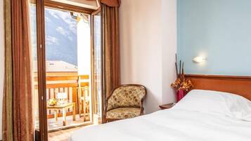 Ein Hotelzimmer mit einem Bett, einem Sessel und Blick auf einen Balkon mit Gartenmöbeln.
