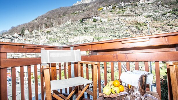 A wooden deck with a table set for a meal, overlooking a vineyard and a hillside with buildings. - Crabun (Pont-Saint-Martin)
