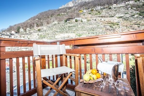 A wooden deck with a table set for a meal, overlooking a vineyard and a hillside with buildings. - Crabun (Pont-Saint-Martin)