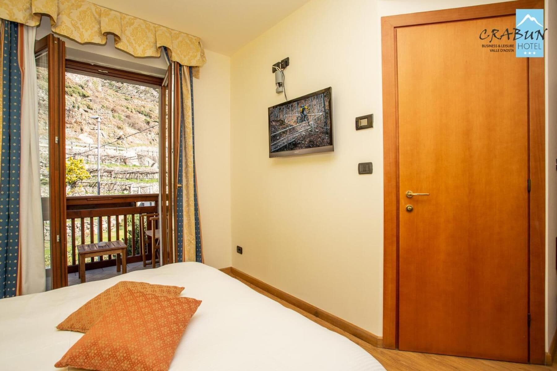 Una habitación de hotel con una cama, una puerta de madera, una ventana con cortinas y un cuadro en la pared.