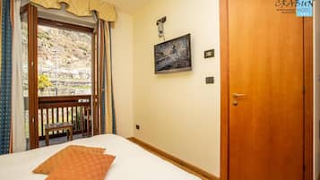 Una habitación de hotel con una cama, una puerta de madera, una ventana con cortinas y un cuadro en la pared.
