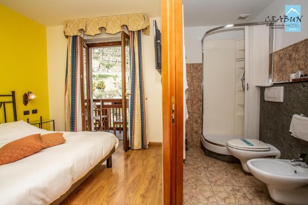 Een hotelkamer met een bed, een houten vloer, een badkamer met douche, twee wastafels en een toilet.