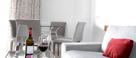 Een moderne woonkamer met een glazen salontafel, een bank met een rood kussen, en een eethoek met een glazen tafel en stoelen.