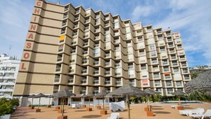 Un hôtel de grande hauteur doté de nombreux balcons, d’un espace piscine avec des chaises longues et de parasols d’extérieur.