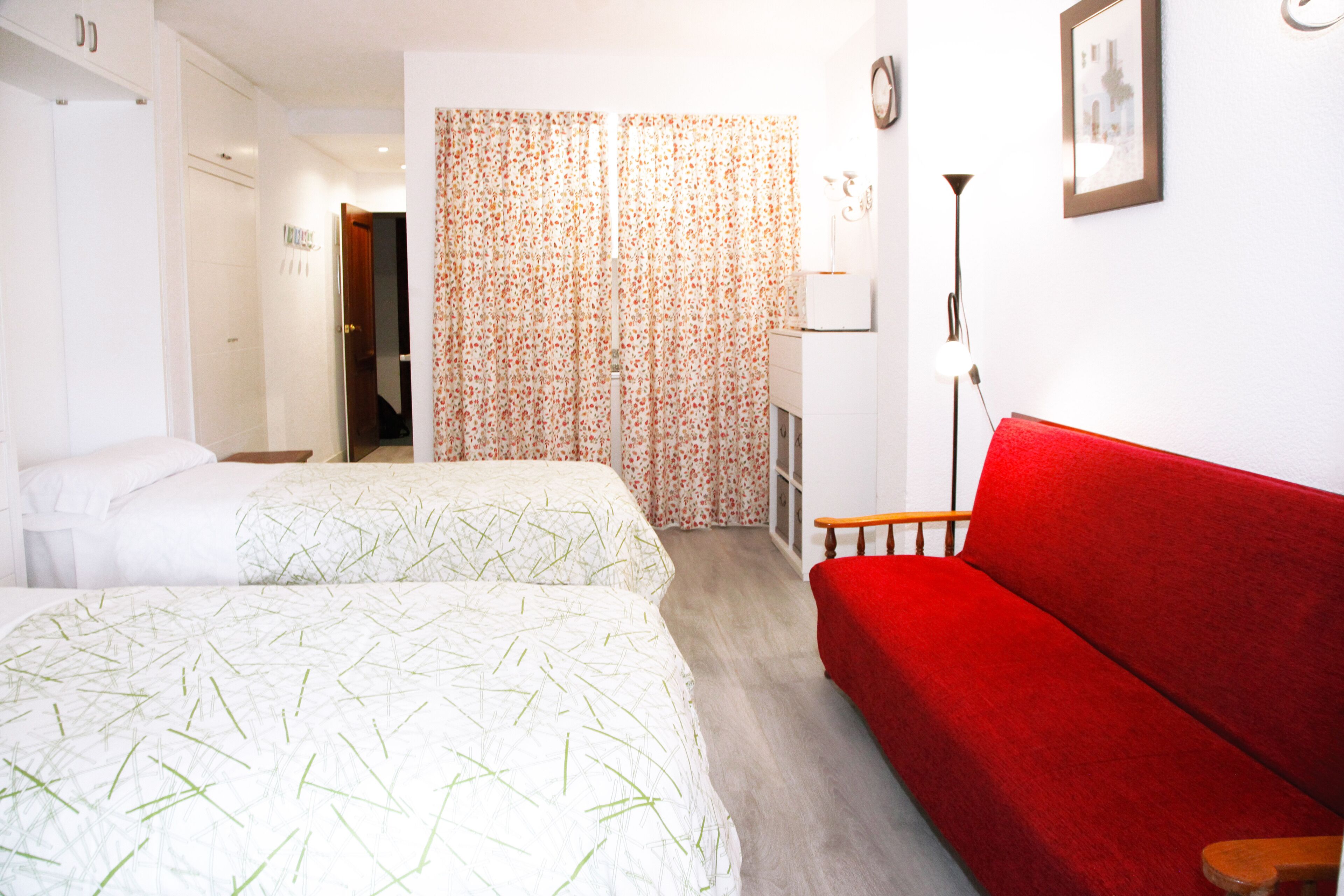 A hotel room with two beds, a red sofa, a lamp, and a framed picture on the wall.