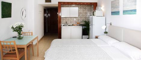 Quarto de hotel com cama, mesa de jantar com cadeiras, cozinha compacta e banheiro visível por uma porta aberta.