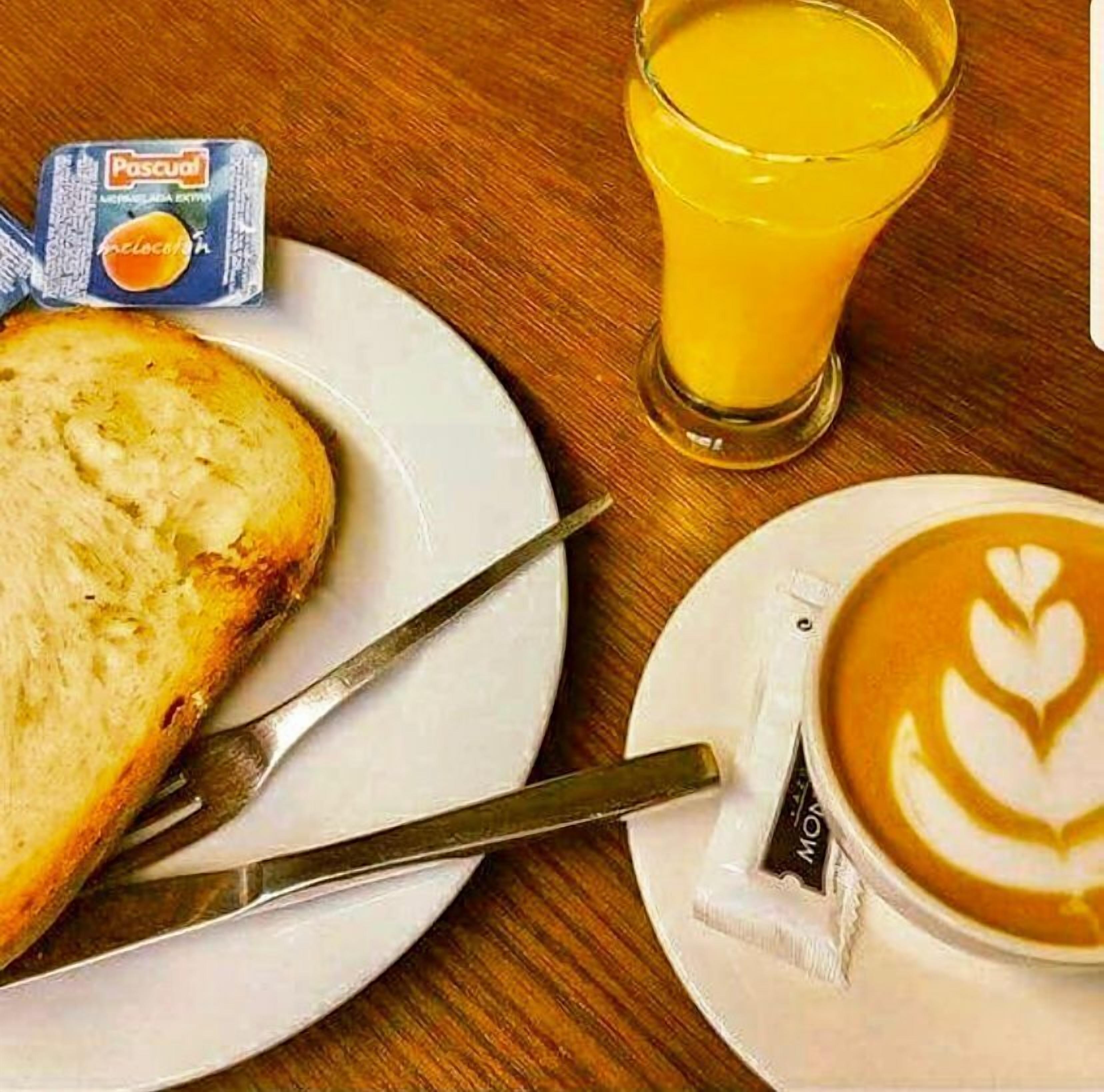 A breakfast setting with toast, a glass of orange juice, and a latte with latte art.