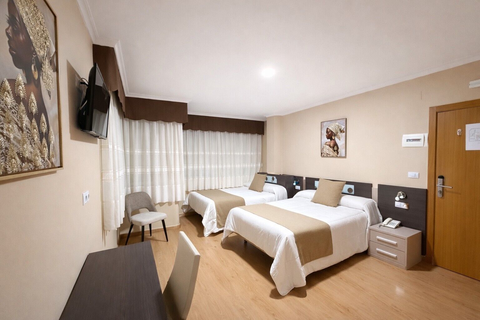 Habitación de hotel con dos camas, un escritorio, una silla, un televisor y una puerta.
