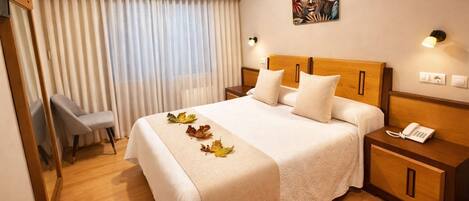 Habitación de hotel con cama, una silla, mesita de noche con teléfono y un cuadro en la pared.