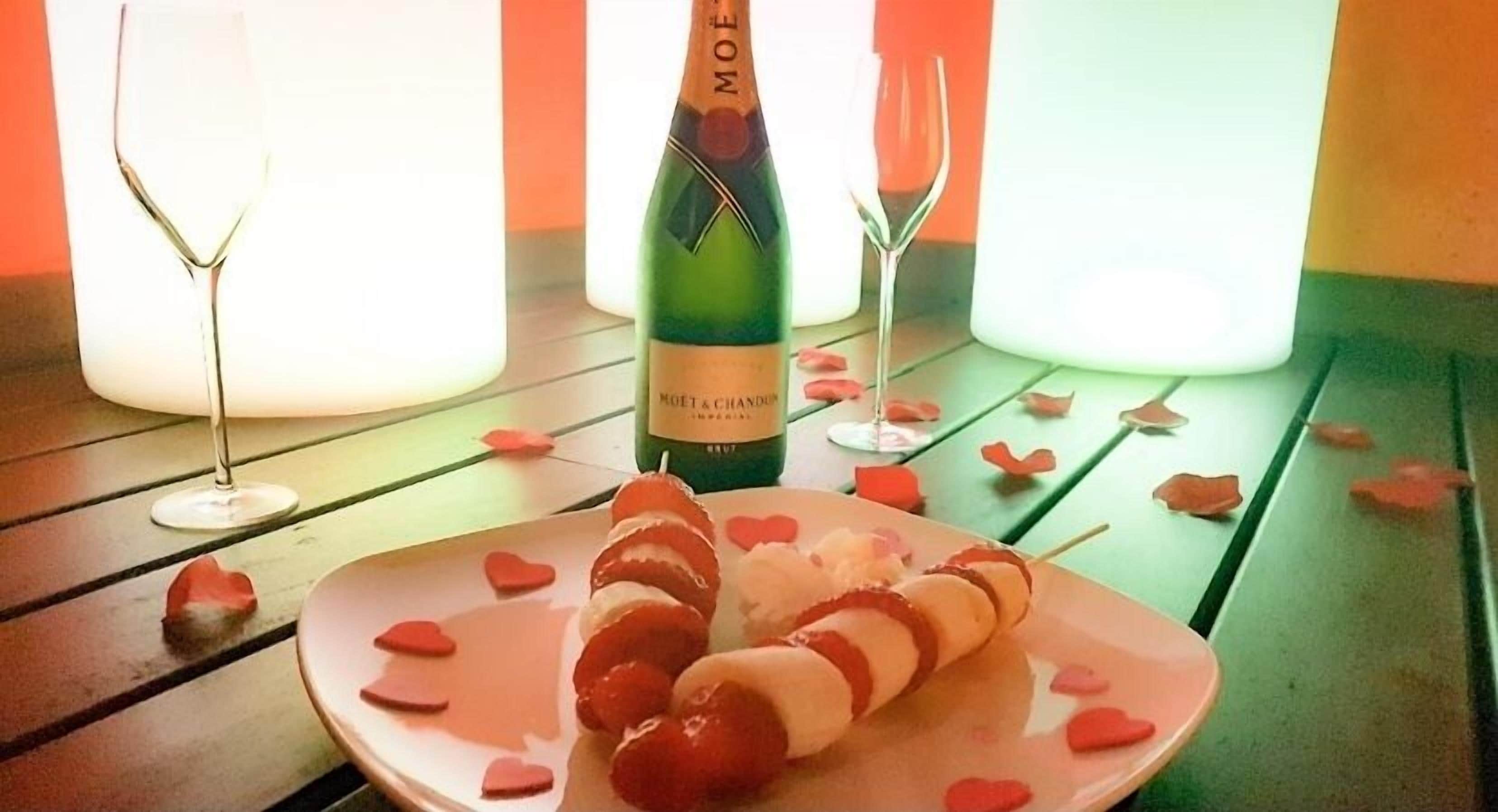 A bottle of Moët & Chandon champagne, a plate with skewers of strawberries and cream, and two empty wine glasses on a wooden table.