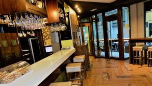 A bar area with a long counter, stools, and a glass display case. - Hotel Galatea (Burela)