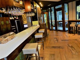 Una zona de bar con una barra larga, taburetes y una vitrina de vidrio.