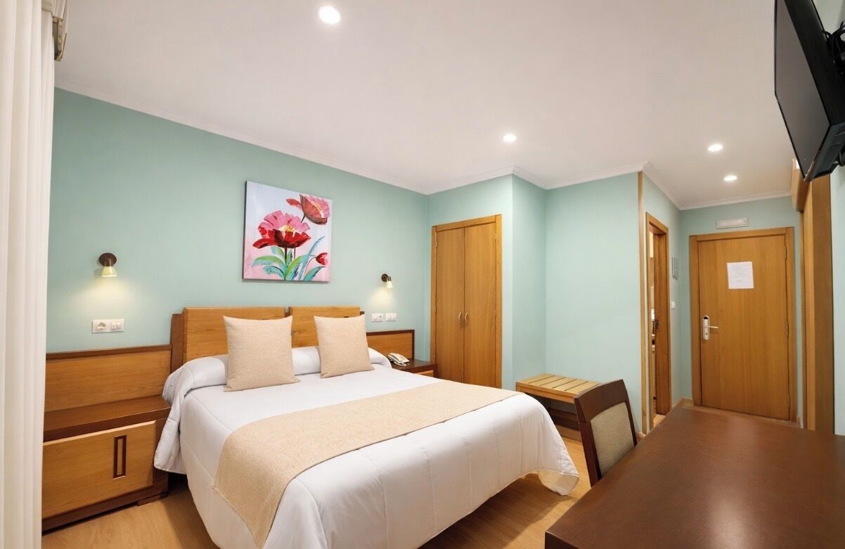 Un dormitorio con cama, mesitas de noche, un armario de madera, un escritorio y una silla.