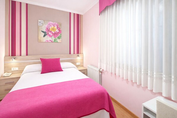 A hotel room with a bed, a nightstand, a wall-mounted painting, and a window with curtains.