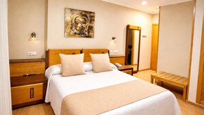 A hotel room with a bed, bedside tables, a wooden bench, a wall-mounted artwork, and a mirror. - Hotel Galatea (Burela)