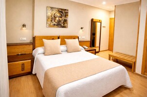 Habitación de hotel con cama, mesitas de noche, un banco de madera, una obra de arte colgada en la pared y un espejo.