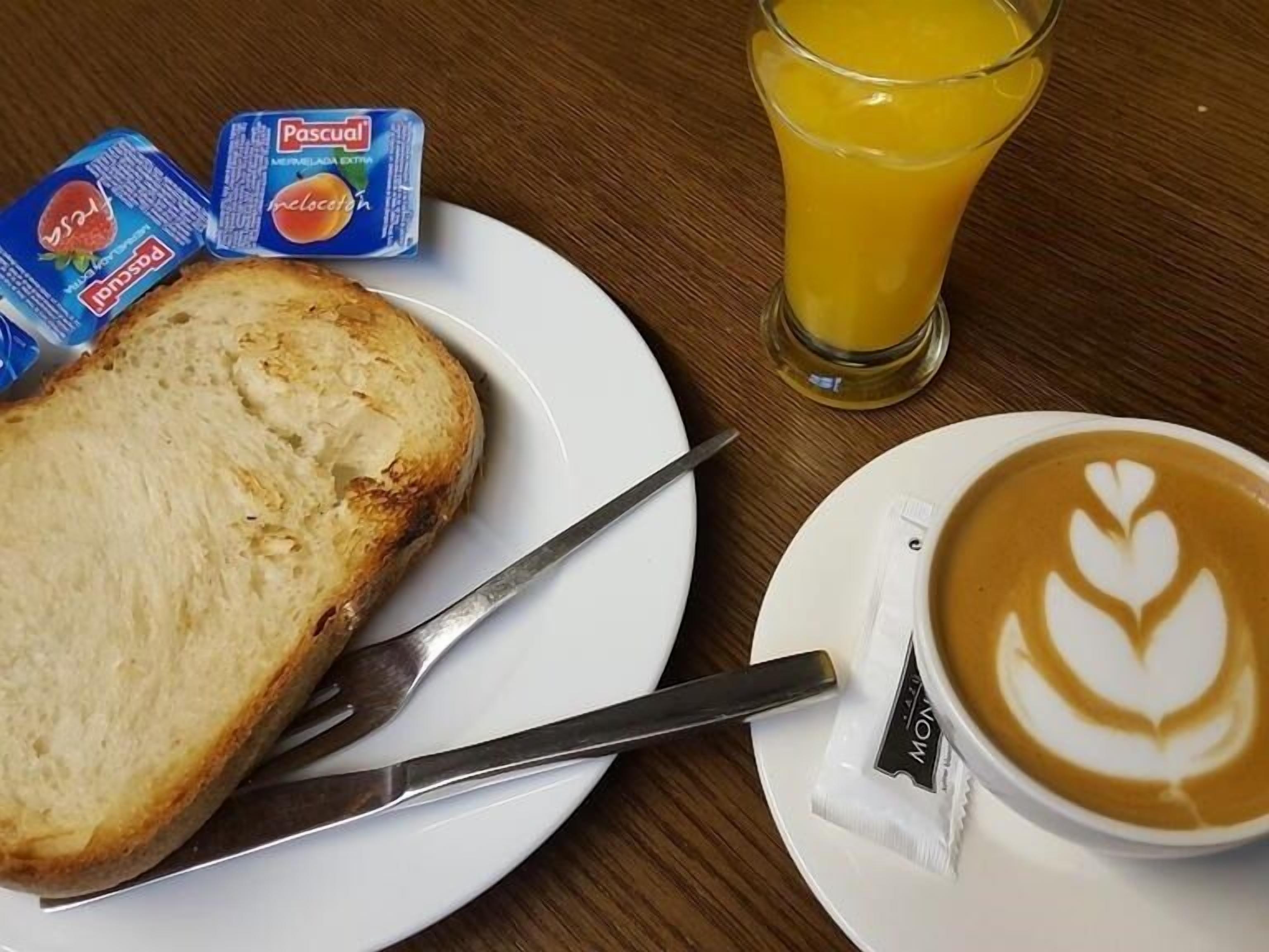 A breakfast setting with toast, Pascal milk, juice, and a latte with latte art.