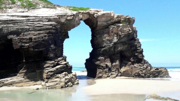 A natural rock formation with a large arch over a beach. - Hotel Galatea (Burela)