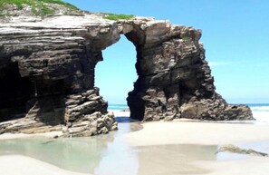 A natural rock formation with a large arch over a beach. - Hotel Galatea (Burela)