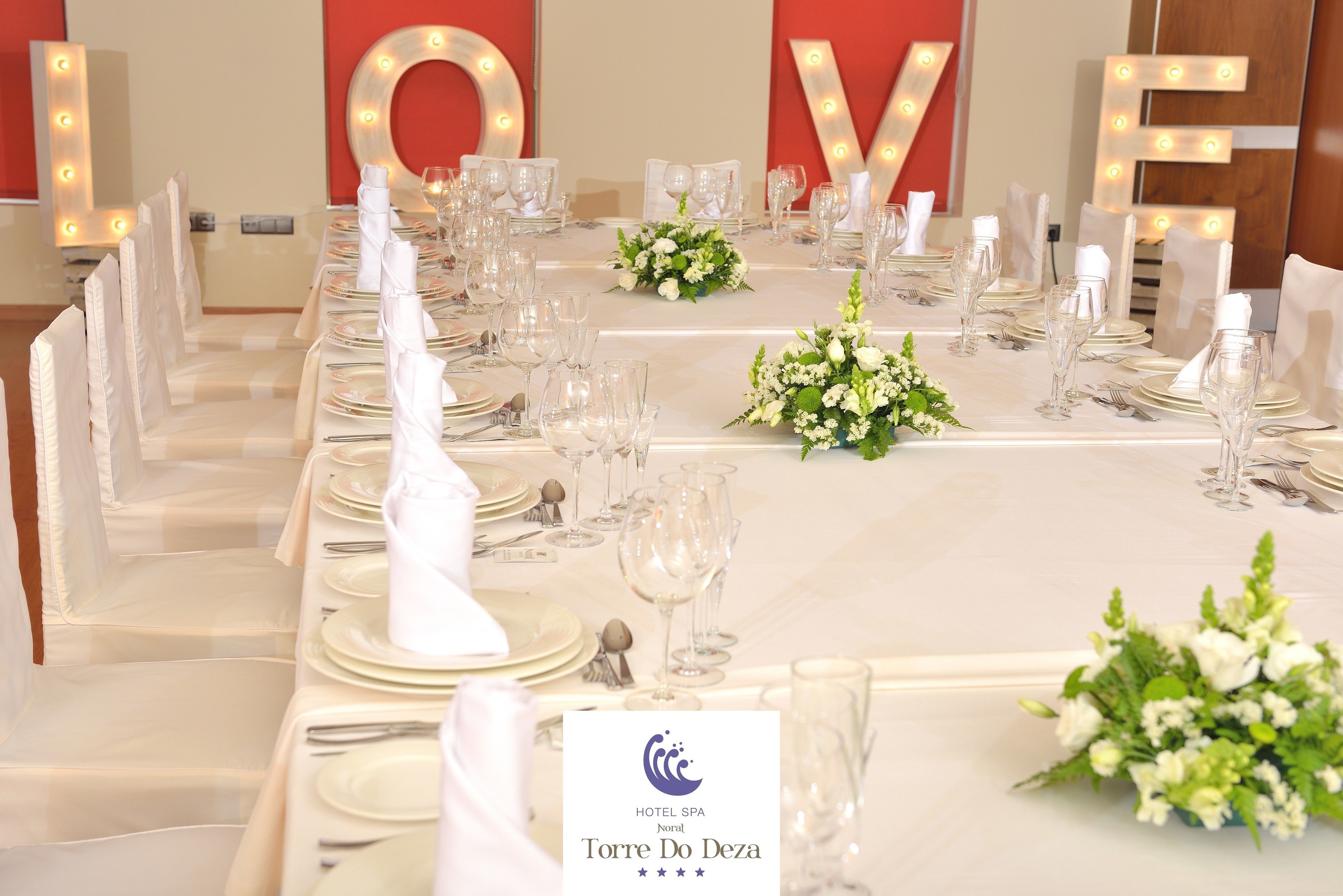 A hotel dining table set with white tablecloths, glassware, and floral centerpieces.
