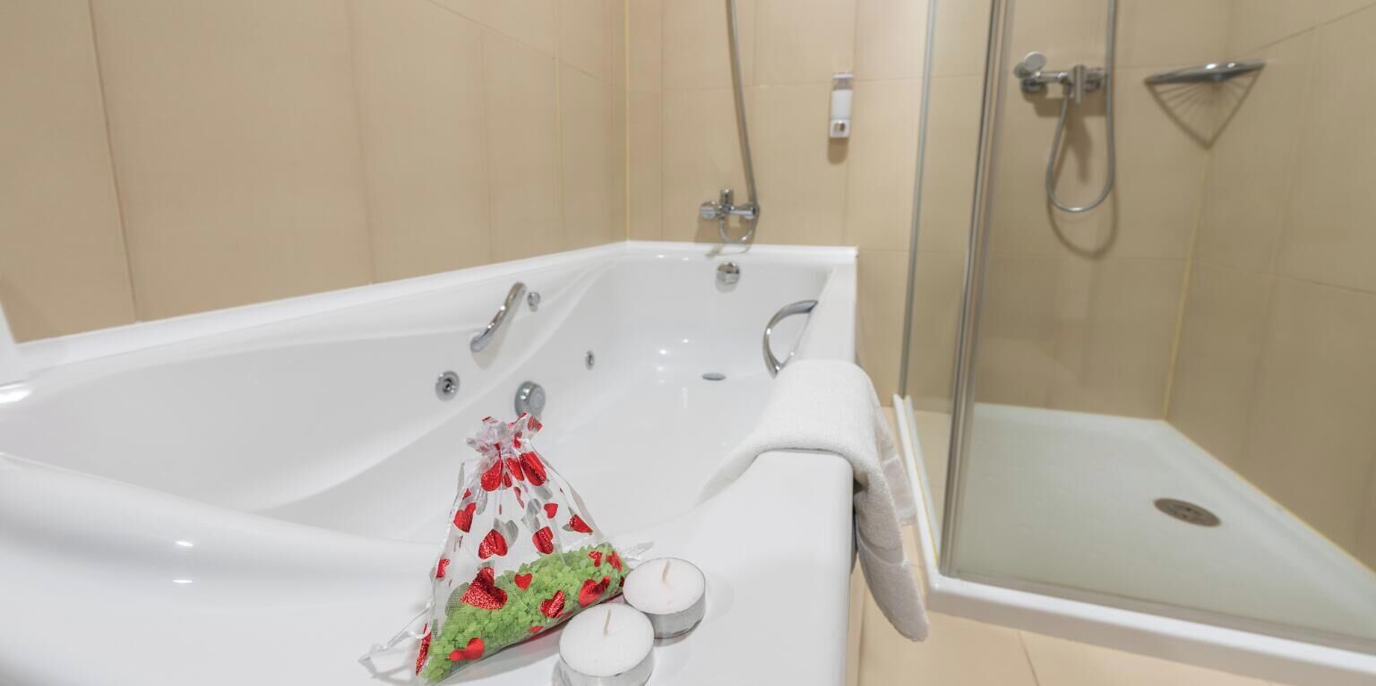 A modern bathroom with a large bathtub, a glass shower enclosure, and a small gift bag with red and green decorations.