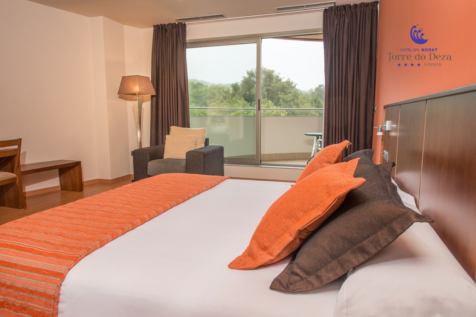 Habitación de hotel con una cama grande, una silla, un escritorio y vistas a zonas verdes por la ventana.