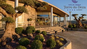 A modern hotel entrance with a large tree and well-maintained landscaping. - Hotel Spa Norat Torre do Deza (Lalin)