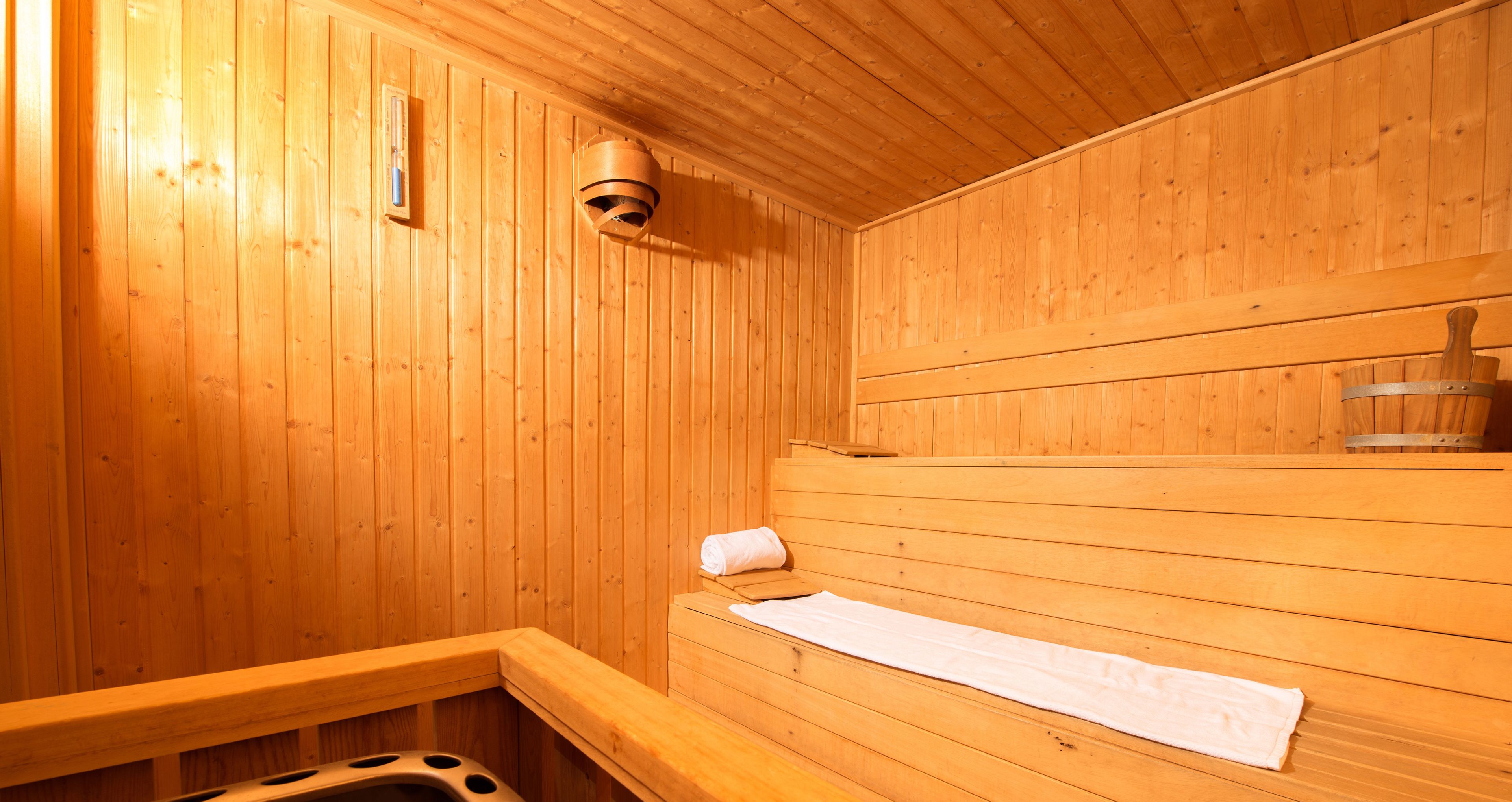 A wooden sauna with benches, a towel rack, and a steam vent.