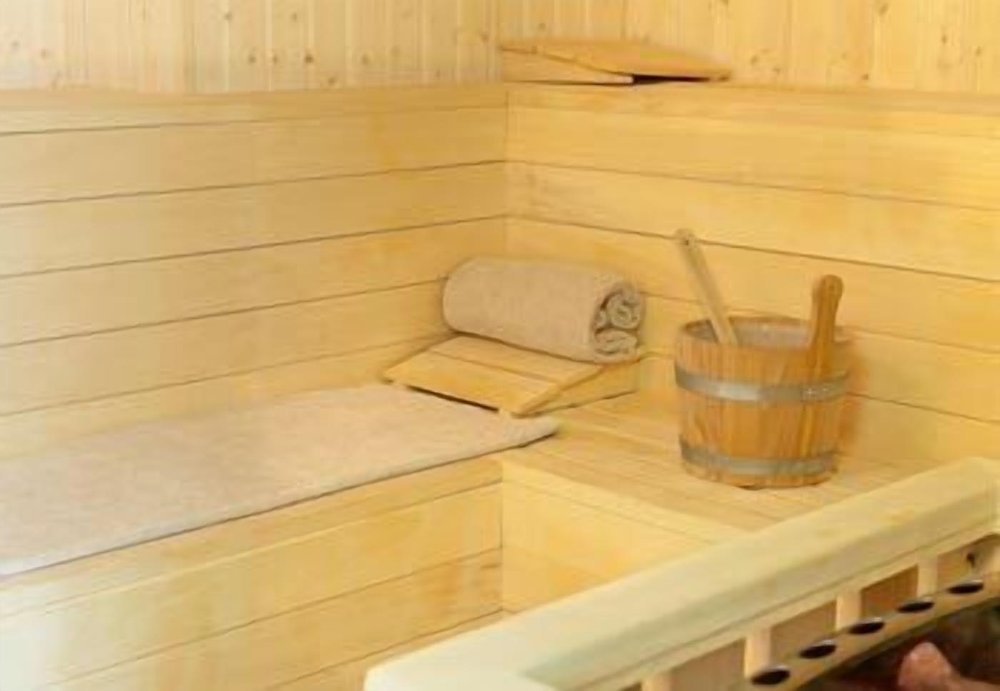 Una sauna de fusta amb bancs, una tovallola i un cubet de fusta.
