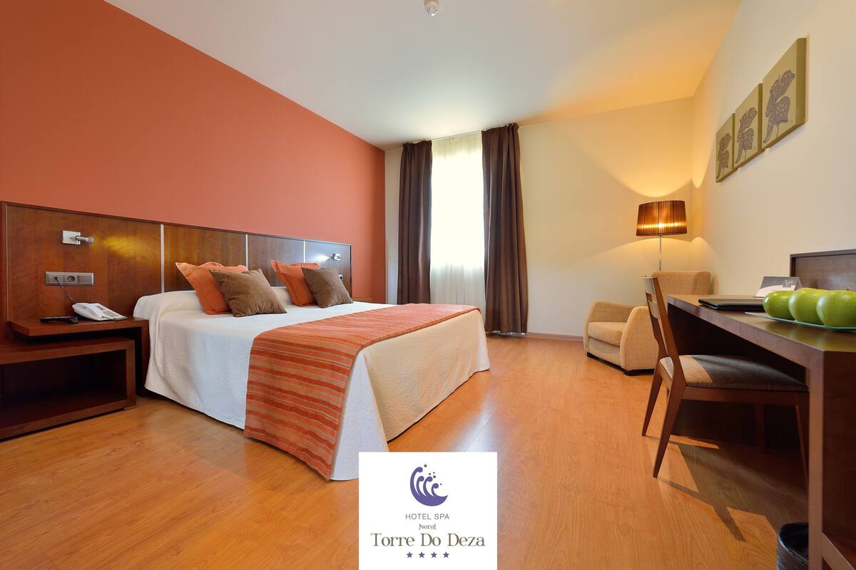 Una habitación de hotel con cama, mesita de noche, lámpara, silla y escritorio con manzanas.