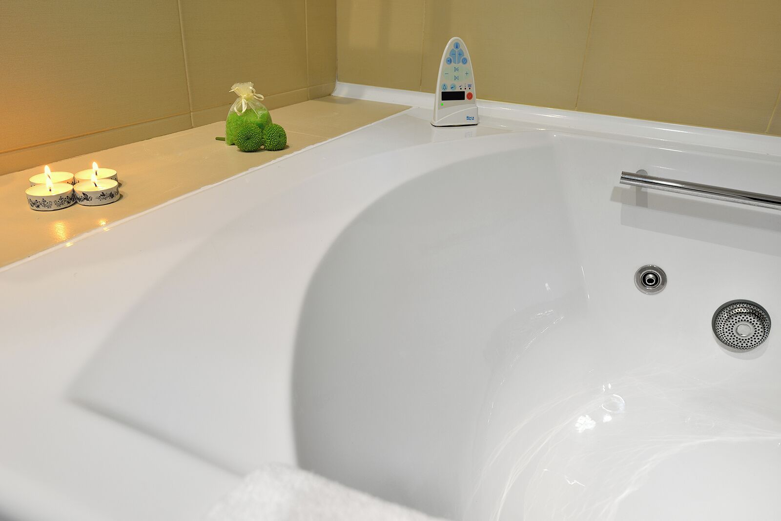 A bathtub with a control panel, a towel, and candles.
