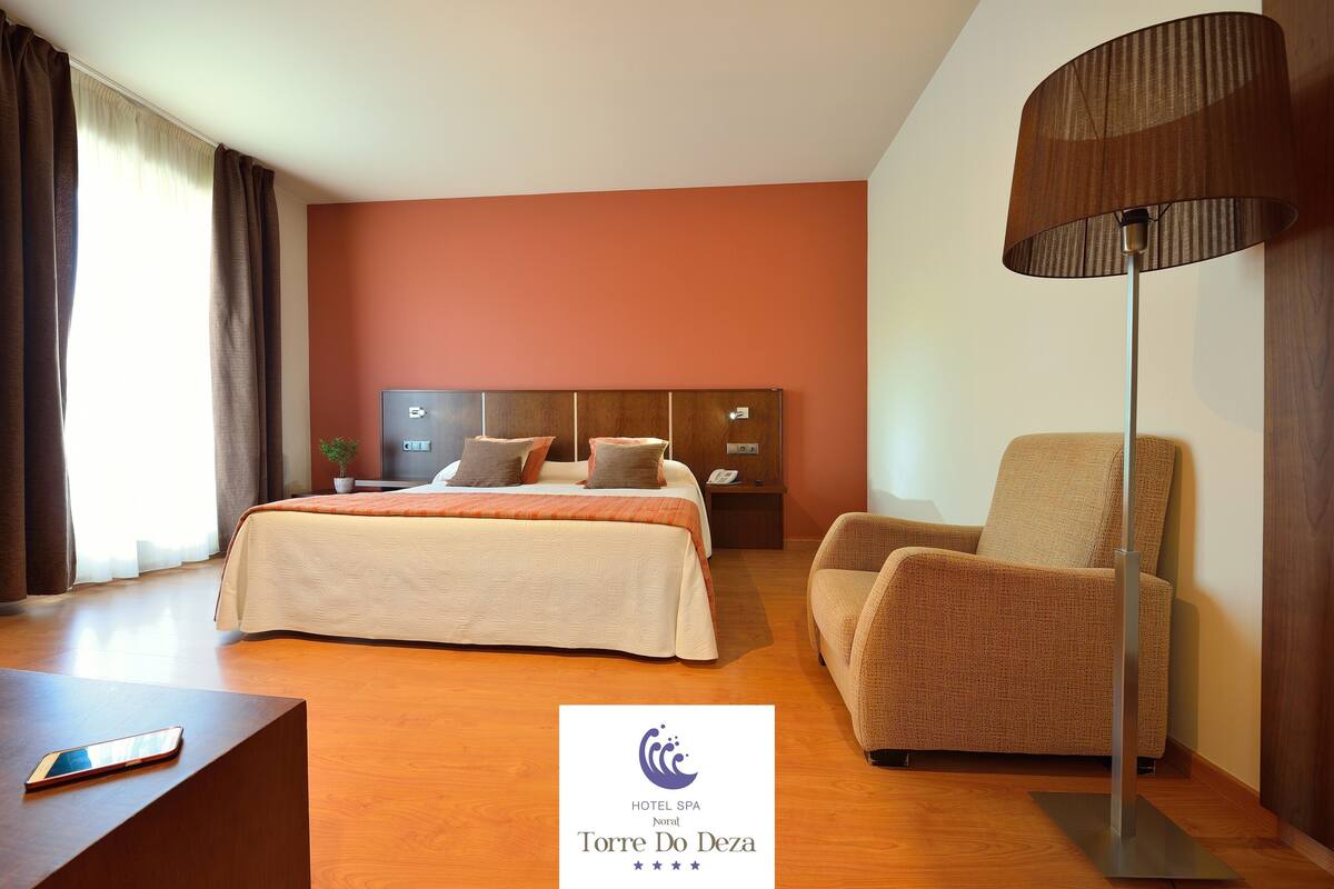 Una habitación de hotel con cama, una silla, un escritorio y una lámpara.