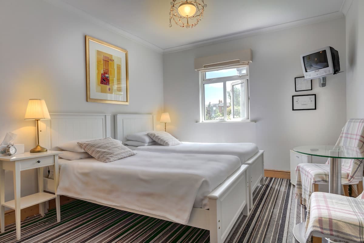 A hotel room with two beds, a glass table, a television, and a window with a view.